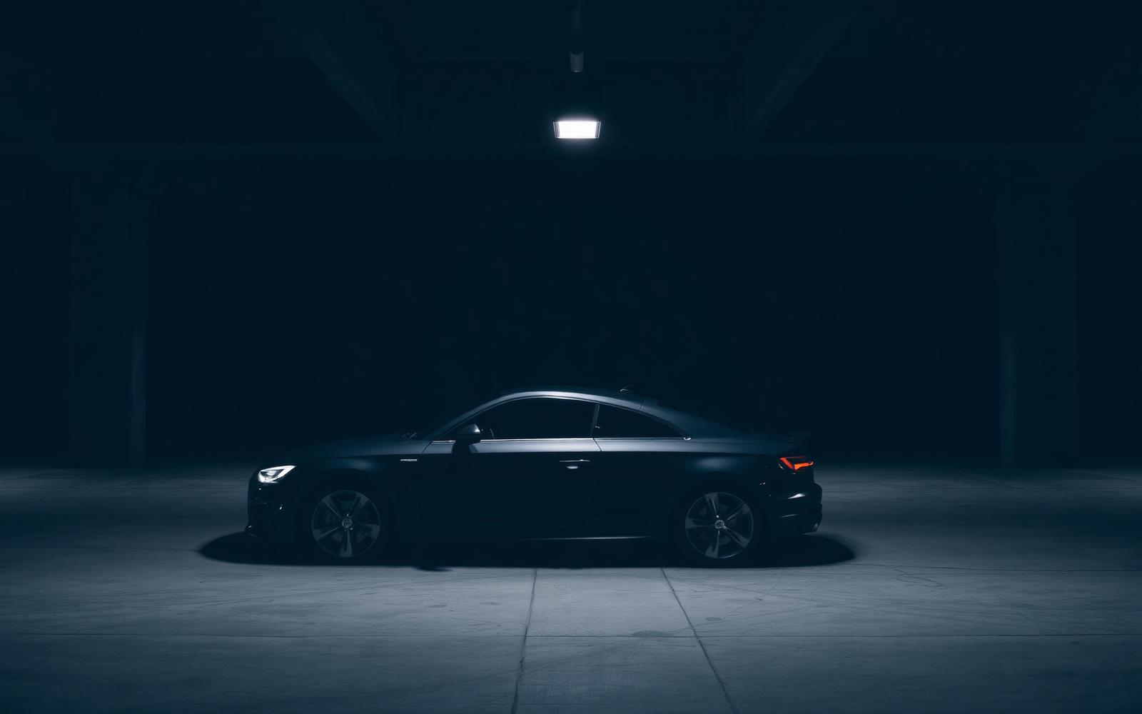 A modern dark car parked in a concrete garage under a single light